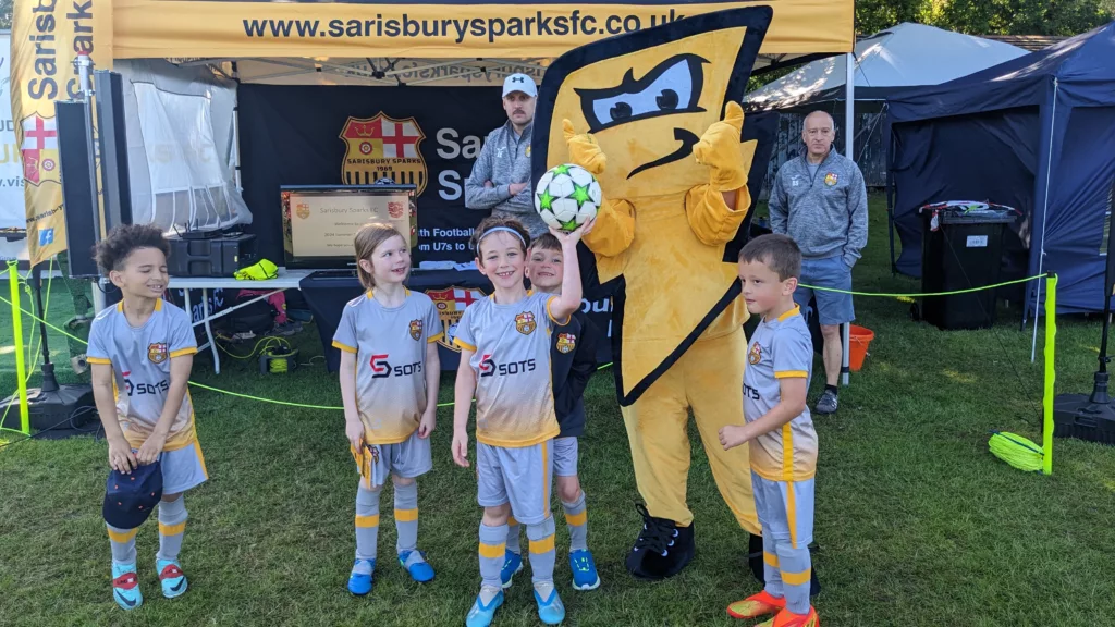 Sarisbury Sparks football players stood on a field with their mascot in their football kits 