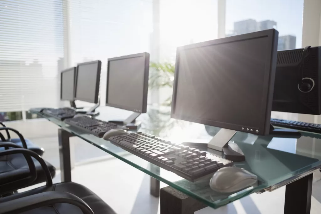 Office computers, lined up on an organised desk in an office building